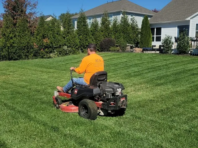 a landscaper mowing a residential lawn on a zero-turn mower