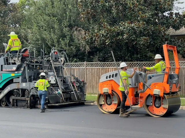 a paving crew with a paver and roller laying asphalt